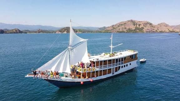 Kapal phinisi berlayar di perairan Taman Nasional Komodo dengan peserta di dek