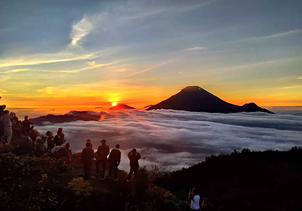 Rombongan pendaki menikmati sunrise di atas lautan awan dengan Gunung Sindoro di kejauhan